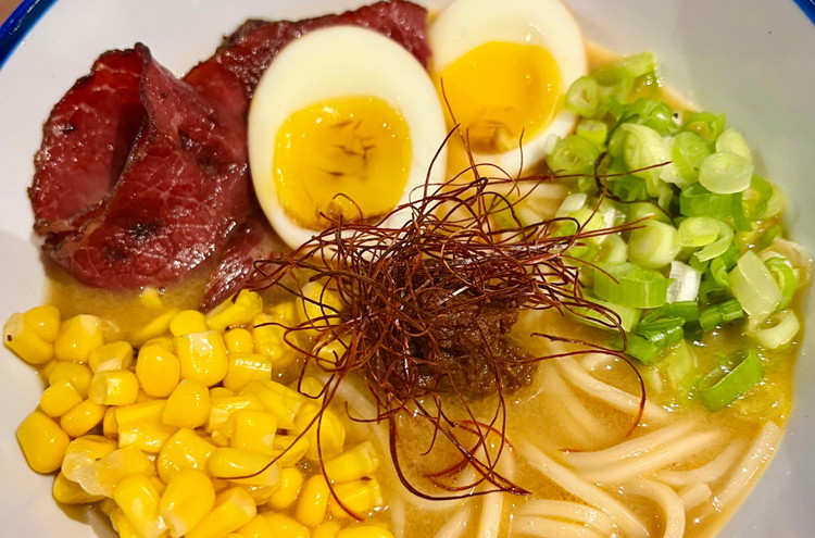 Image of Eihälften, Pastrami, Mais, Frühlingszwiebeln, Miso Paste und Chili Fäden dekorativ auf die Ramen legen.
