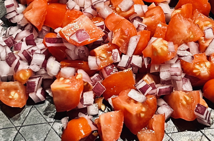Image of Erhitze eine Pfanne und brate die fein gehackten Zwiebeln sowie die klein geschnittenen Tomaten darin an.