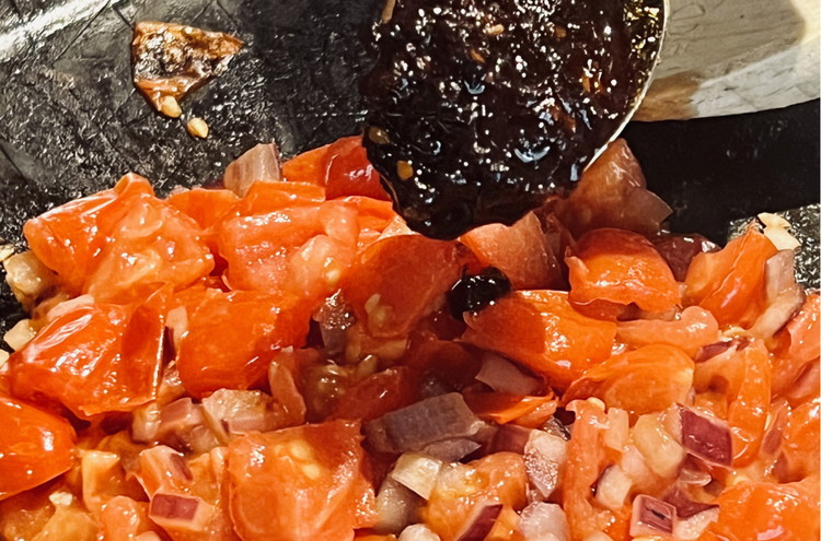 Image of Füge 2 Esslöffel TADA Spice Up Würzpaste hinzu und vermische sie gut mit den angebratenen Zwiebeln und Tomaten.