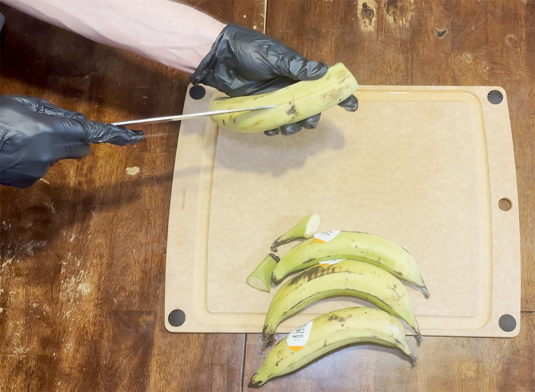 Image of Cut the ends off of the plantains. Take a knife and gently slice through the skin of the plantain trying not to hit the inner portion. Peel the skin off of the plantains and discard.