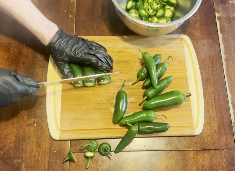 Image of Wearing rubber gloves slice off the stem end of all the jalapenos. Discard stem ends.
