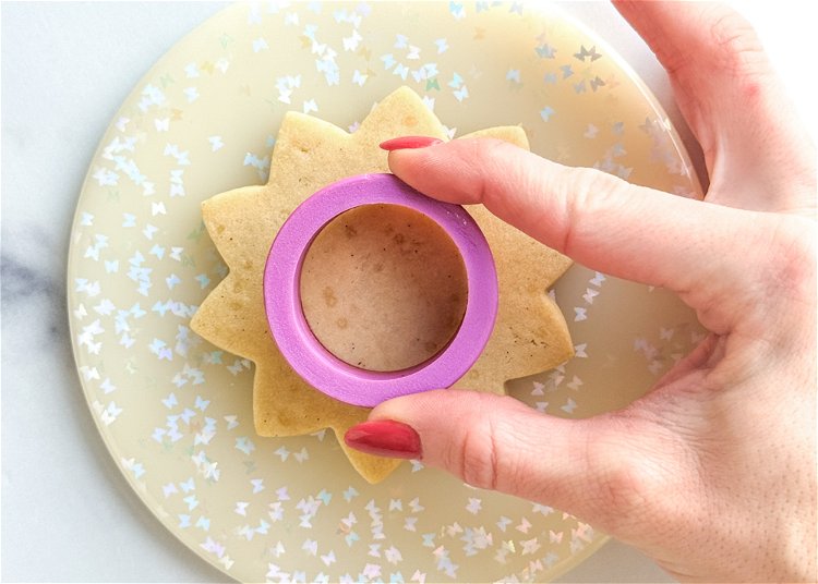 Image of Using a 1.5” circle cookie cutter, gently push the cutter into the center of the cookie, turning the cutter in either direction to make a circular impression on the cookie. You can also use a small drinking glass or the circular side of a piping tip to create a circle. The purpose of this is just to score the cookie, so that you have a guide while you’re piping. 