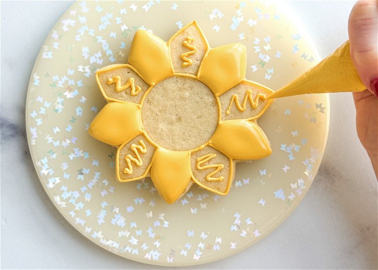 Image of Once the icing has crusted over, repeat step 5, piping a squiggle of yellow outline consistency icing, on the remaining petals. 