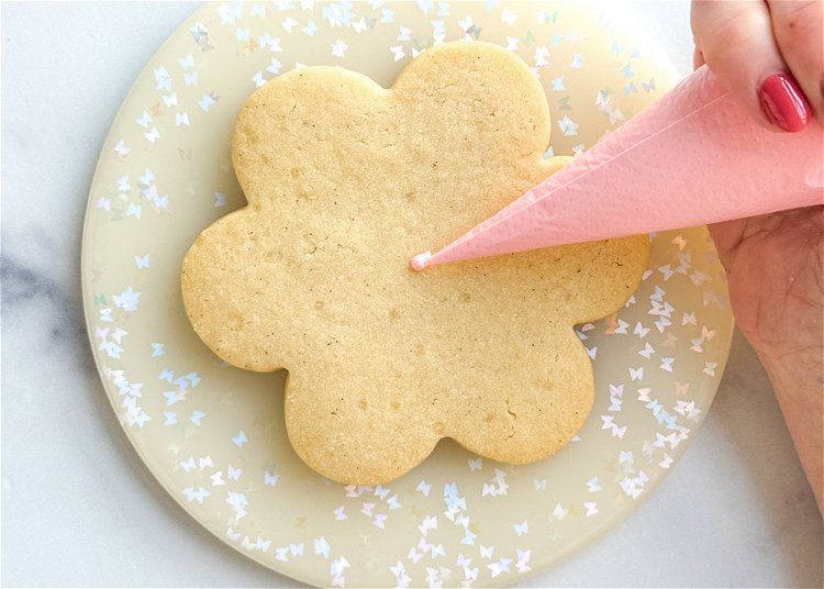 Image of Using the pink outline consistency icing, pipe a small dot of icing in the center of the cookie. This will help anchor your design and give you a center point to start and end your flower petals from. 