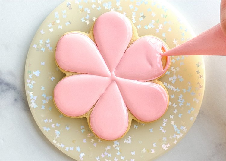 Image of Flood the three alternating petals with the pink flood consistency icing. Let these sections dry for 20-30 minutes, or until crusted over, before moving onto the next step. It may help to place your cookies under a fan to speed the drying process. 