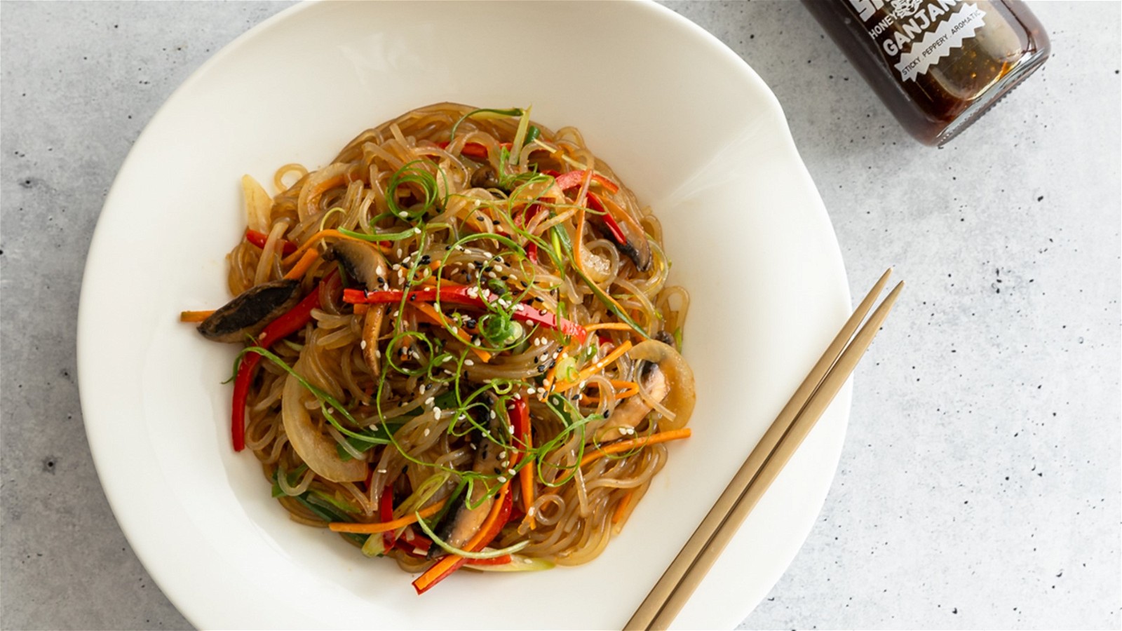Bowl of Honey Pepper Japchae with bottle of Sauce