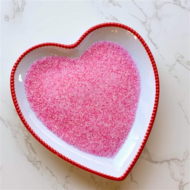 Image of Prepare your sanding sugar. Sanding sugar has larger grains than granulated sugar, but you can use granulated sugar for a finer texture. To prepare your sanding sugar, add about ¼ cup sanding sugar into a Ziploc bag. Add a small drop of Bubblegum Pink Gel Food Coloring to the mix, seal the bag, and gently mix the ingredients by mashing the bag around until the food coloring is fully incorporated. See our full colored sanding sugar tutorial here.  Once you have made your sanding sugar, place it into a shallow dish or bowl.  
