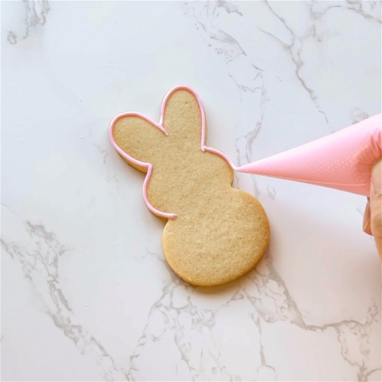 Image of Outline the entirety of the bunny shape with pink outline consistency icing. 