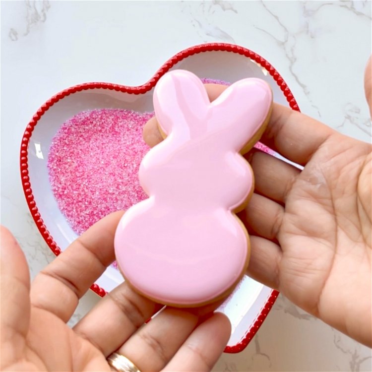 Image of While the icing is still wet, gently drop the bunny wet icing side down into the shallow dish of colored sanding sugar. 