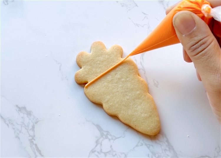 Image of Outline the carrot shape, except for the top, with orange outline consistency icing.  