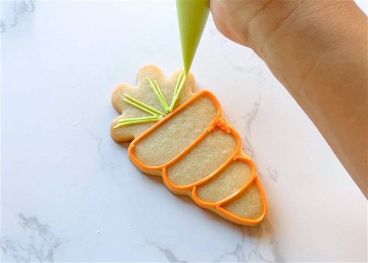Image of Using the shape of the carrot cookie cutter as a guide, outline the 4 sections of the carrot with orange outline consistency icing. 