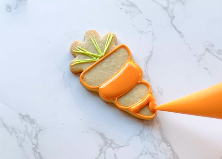 Image of Using orange flood consistency icing, fill in the bottom section of the carrot and the middle section. Be sure to flood adjacent sections at different times, and you want the icing to dry slightly before flooding adjacent sections. This prevents the two sections from bleeding into each other. 