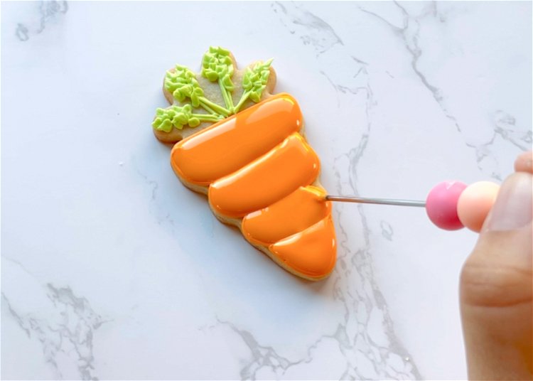 Image of Fill in the remaining two sections of carrot with orange flood consistency icing, and gently move the icing around with a scribe tool or toothpick to pop any air bubbles and to ensure full coverage. 