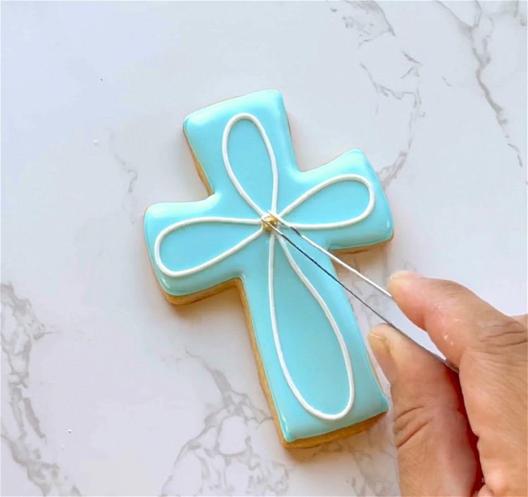 Image of Using offset tweezers, place a gold pearl sprinkle at the intersection of white lines, in the center of the cross. Alternatively, you can add a dab of white outline consistency icing there to look like a pearl. 