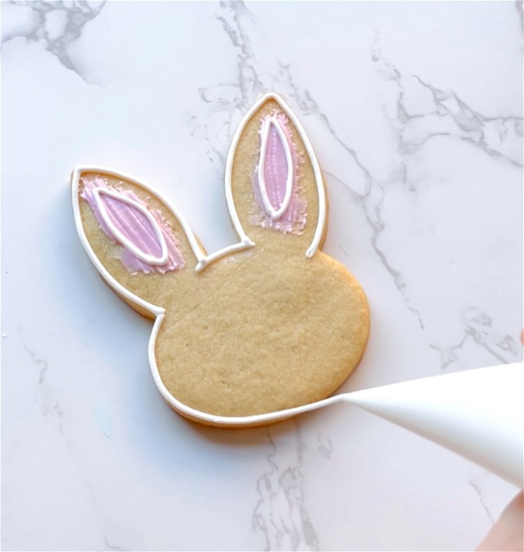 Image of Next, outline the outside of the bunny shape with white outline consistency icing. 