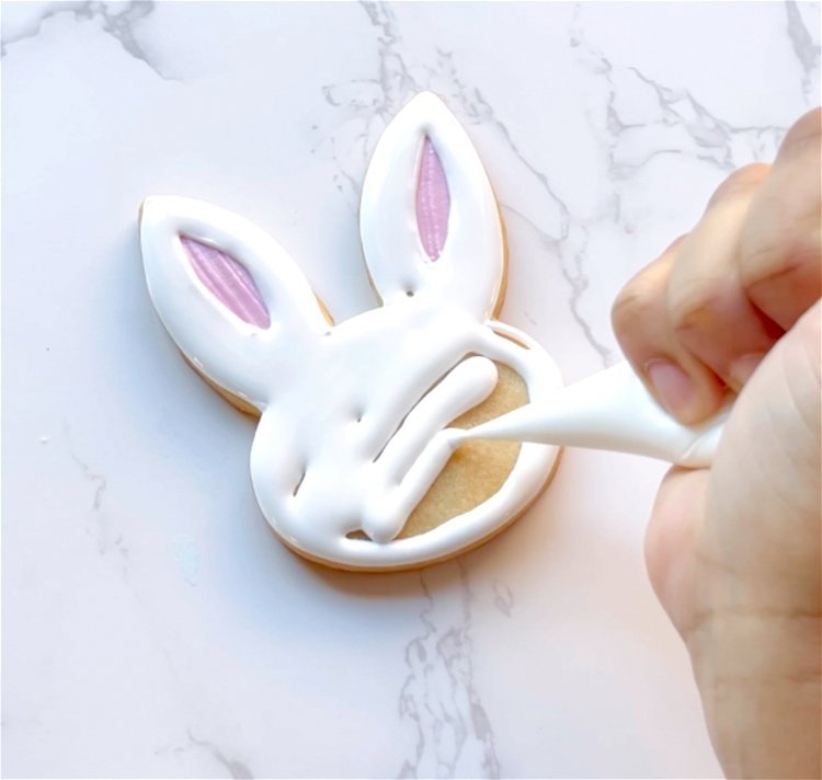 Image of Fill the rest of the bunny face with white flood consistency royal icing, gently moving the icing around with a toothpick or scribe tool to ensure full coverage and to pop any air bubbles. 