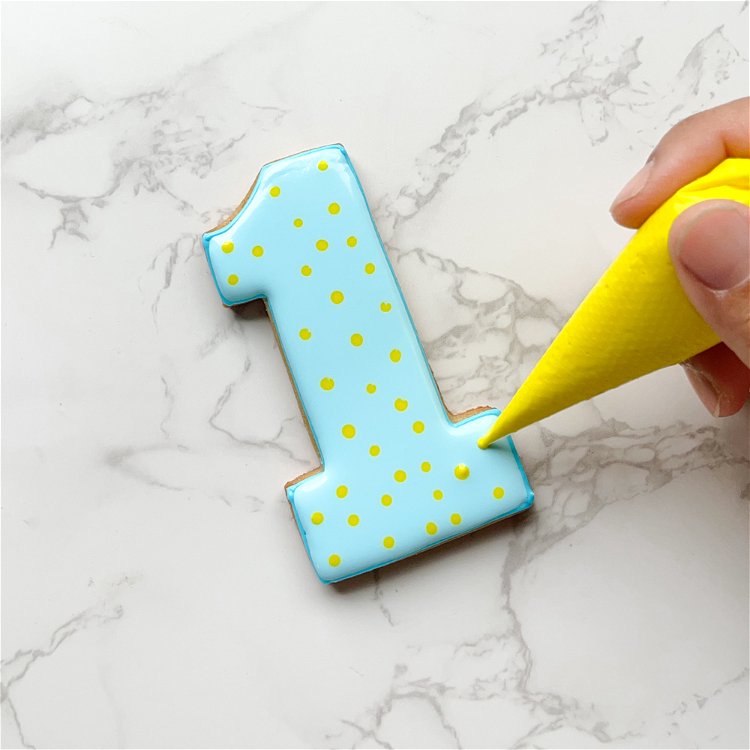 Image of Pipe dots of yellow icing throughout the shape. By doing this when the base icing is still wet, the yellow dots will blend into the blue icing, creating a patterned base. 