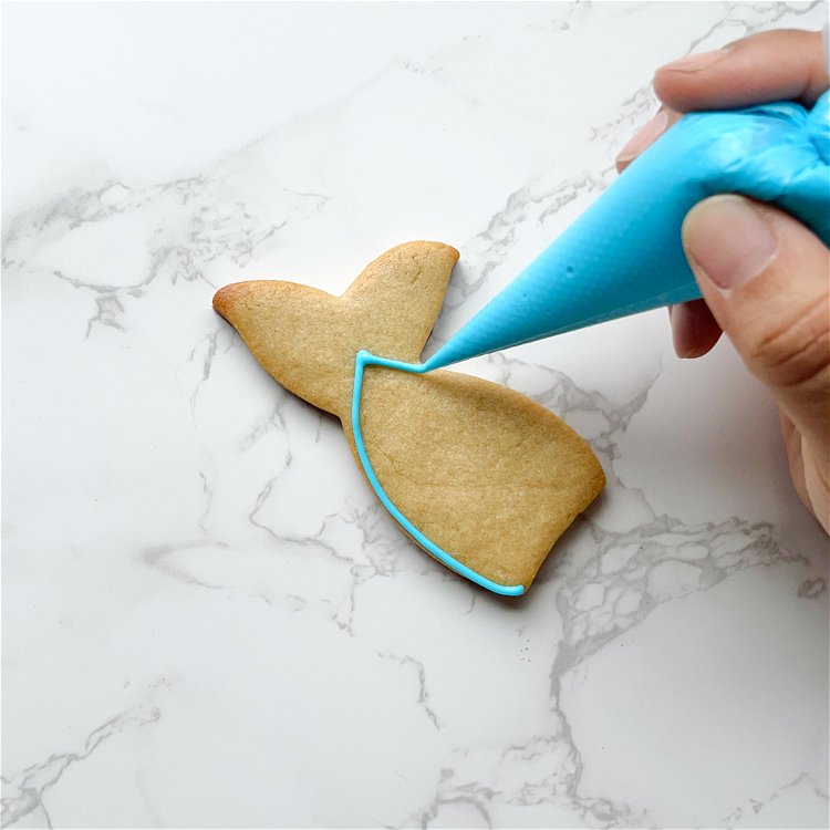 Image of Outline the main section of the mermaid tail with teal outline consistency icing.