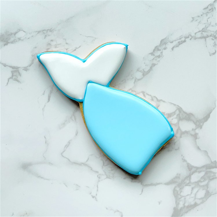 Image of Once the white fins are crusted over, flood the main part of the tail with light blue icing. Use a scribe tool or toothpick to gently coax the icing to ensure full coverage and to pop any air bubbles. 
