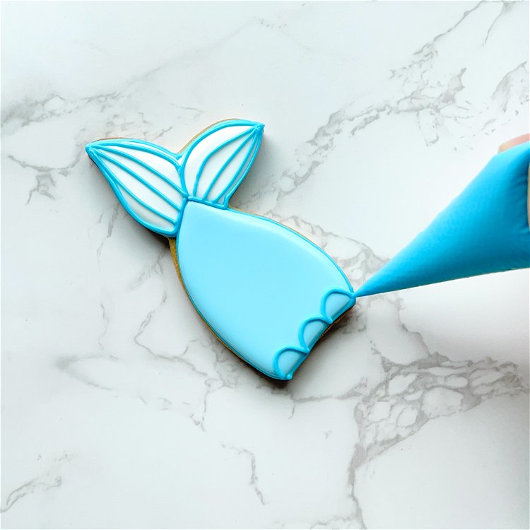 Image of Using ocean teal outline consistency icing, pipe a scalloped pattern. Start at the widest part of the body of the cookie and repeat the pattern as you move down toward the fins.  