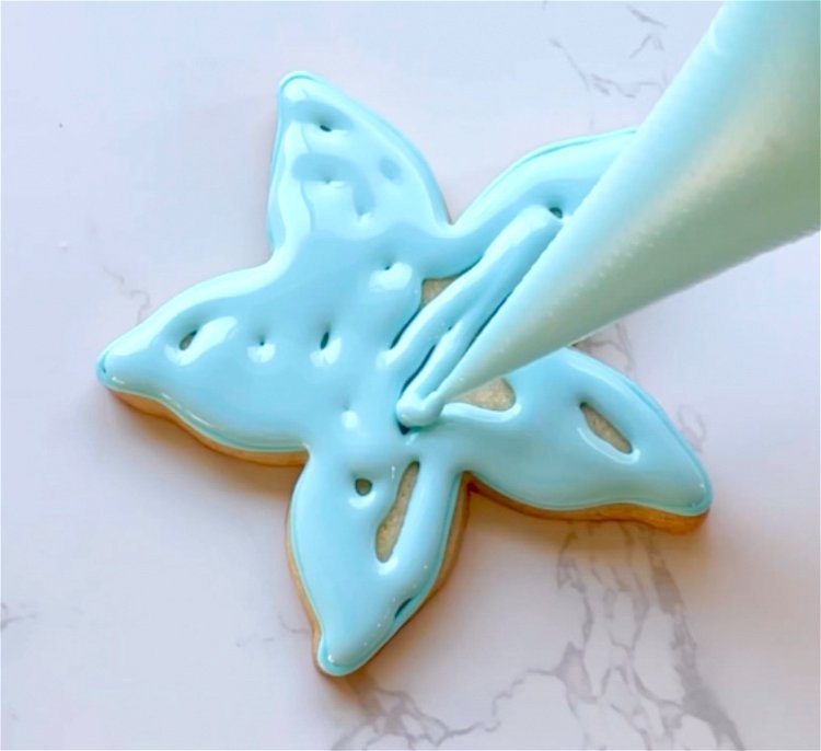 Image of Flood the starfish shape with sky blue flood consistency icing.  Wait for this base flood to dry for 30-60 minutes, or until just crusted over. Placing cookies under a fan may help to dry the icing more quickly. 