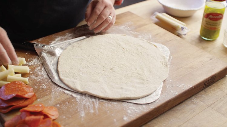Image of Slide the pizza dough onto a well-floured pizza peel.