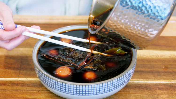 Image of Pour the tea brine into a nonreactive container. Take the eggs out of the ice water and soak them in the tea brine. Make sure everything is well-immersed. Leave them in the fridge for at least 24 hours before eating.