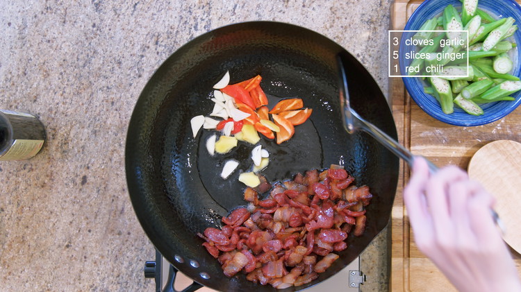 Image of When you see some fat (about 2 tbsps) is rendered out, push the cured meat to the side and toss in some garlic, ginger slices, and red chilies. Stir for a minute or until fragrant.