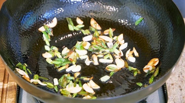 Image of Add a generous amount of cooking oil to a wok, along with the scallions and garlic slices. Stir over low heat until the aromatics are lightly golden, which will take about 3 minutes.