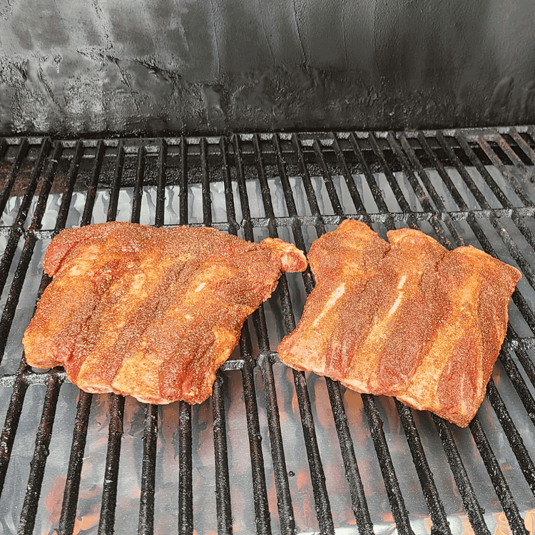 Image of Smoke the Ribs: Once the smoker is at the right temperature, place the ribs directly on the grate, bone side down. Close the lid and let them smoke for about 2 hours. Maintain a steady temperature throughout the smoking process.