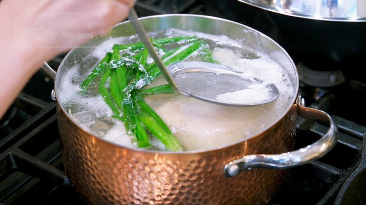 Image of By now, the chicken pot should have come to a boil. Skim off the scum that is floating on top of the water. Switch the heat to low and continue to cook the chicken for 8 more minutes.