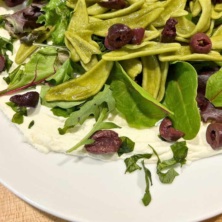 Image of Top yogurt with one cup spring mix, half of the cooked pasta, and half of the chopped olives. Drizzle with half of the vinaigrette.