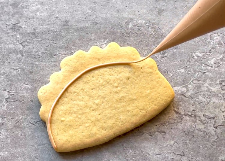 Image of Using the light brown outline consistency icing, outline a half-circle shape. This will be the taco shell. Be sure not to outline the section for the toppings at the top of the shape.  