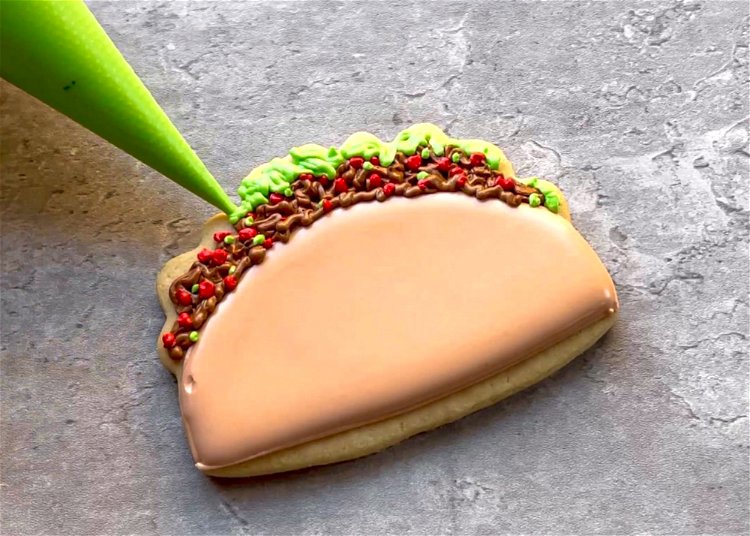 Image of Continue using your green outline consistency icing to pipe “lettuce” at the very top of the shape. You can pipe in lines, moving outward toward the edge of the cookie, to create the illusion of shredded lettuce.  