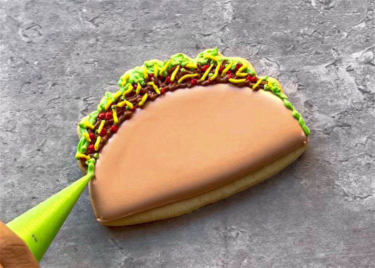 Image of Add a bit more green to the lower edges of the taco, so that the toppings reach all of the way to the base of the cookie. 