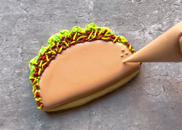 Image of To create a textured taco shell, pipe dots of light brown outline consistency icing near the edges of the taco shell. 