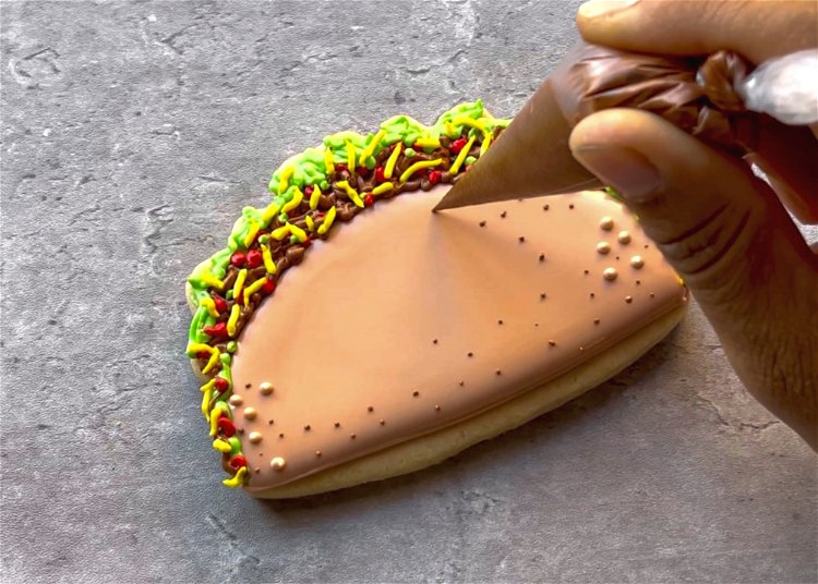 Image of For even more texture, pipe a few small dots of dark brown outline consistency icing throughout the body of the taco shell. 