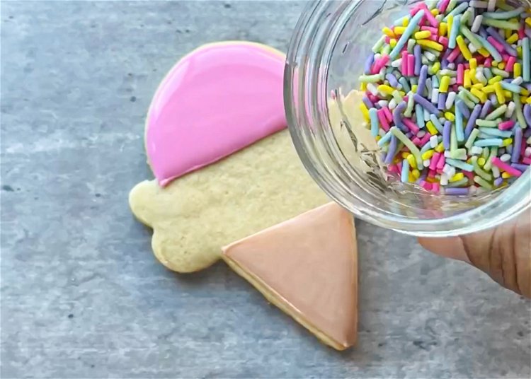 Image of While the pink icing is still wet, add sprinkles to the top of the cone. 