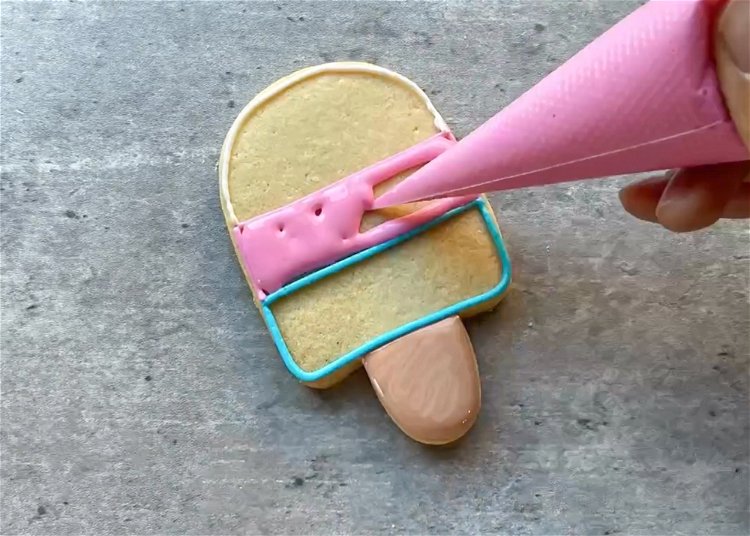Image of Using your pink flood consistency icing, fill in the middle pink section of the popsicle. Use a toothpick or scribe tool to coax the icing to the edges and to pop any air bubbles. 