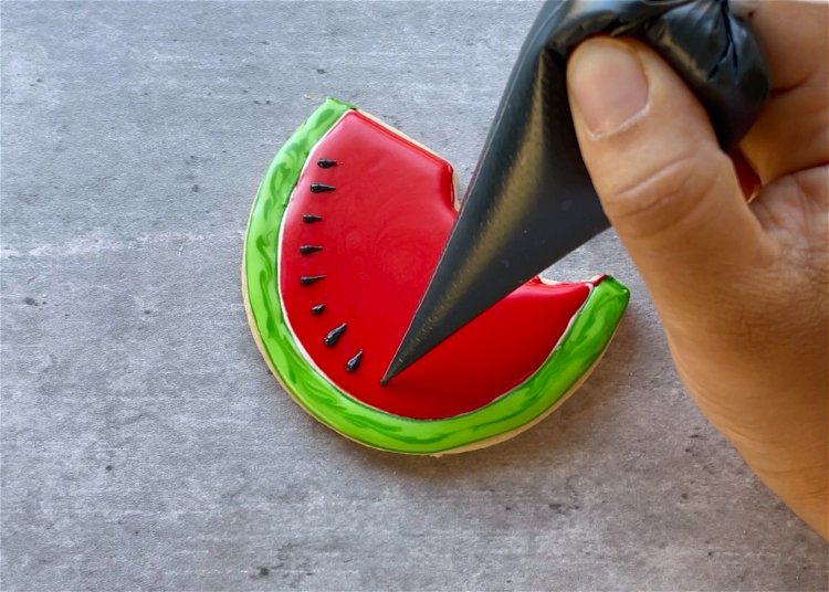 Image of Once the red icing is just crusted over, add your black watermelon seeds. Waiting until the red is crusted over will ensure that there is good definition between the red flesh of the watermelon and the black seeds. Use a scribe tool to gently pull the black seeds to give them their distinctive point. 