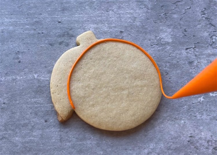 Image of Use your orange outline consistency icing to outline the circular orange. Be sure not to outline the leaf or stem. 