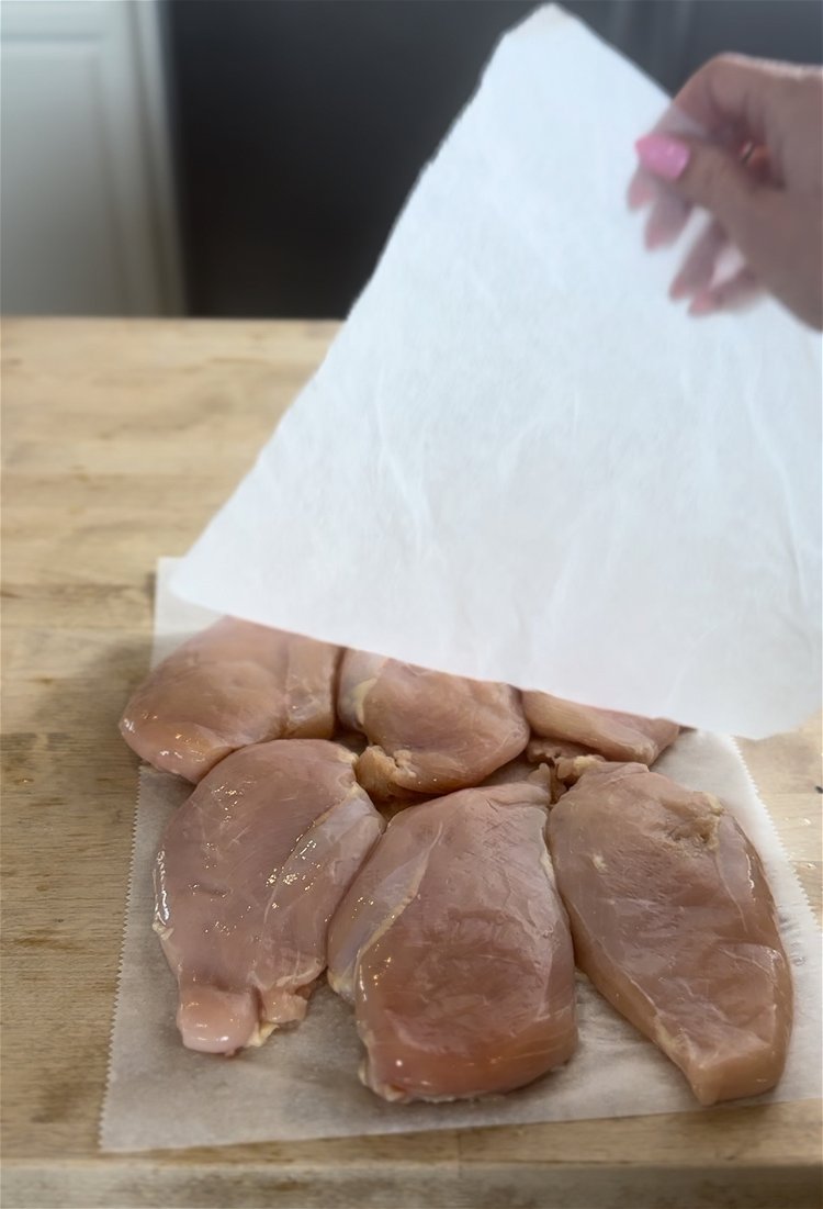 Image of Take chicken and place between two pieces of parchment paper...