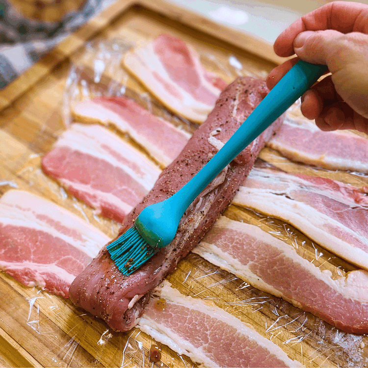 Image of Lay out 5 strips of bacon, and lay one loin on it, brush with some of the glaze, then wrap the boar tenderloin fully with the bacon strips.