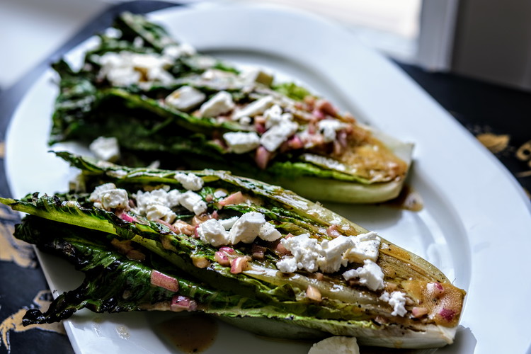 Image of Plate the lettuce cut side up.  Spoon vinaigrette generously over the lettuce, including shallots.  Spread crumbled feta cheese over the lettuce and serve.