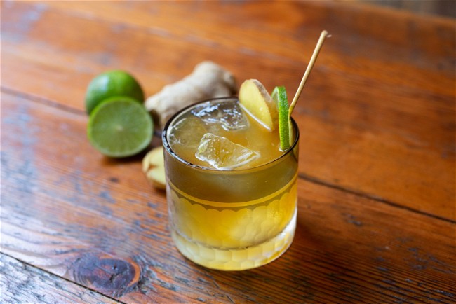 A short glass cocktail featuringa delicious amber liquid, garnished with coins of ginger and lime.