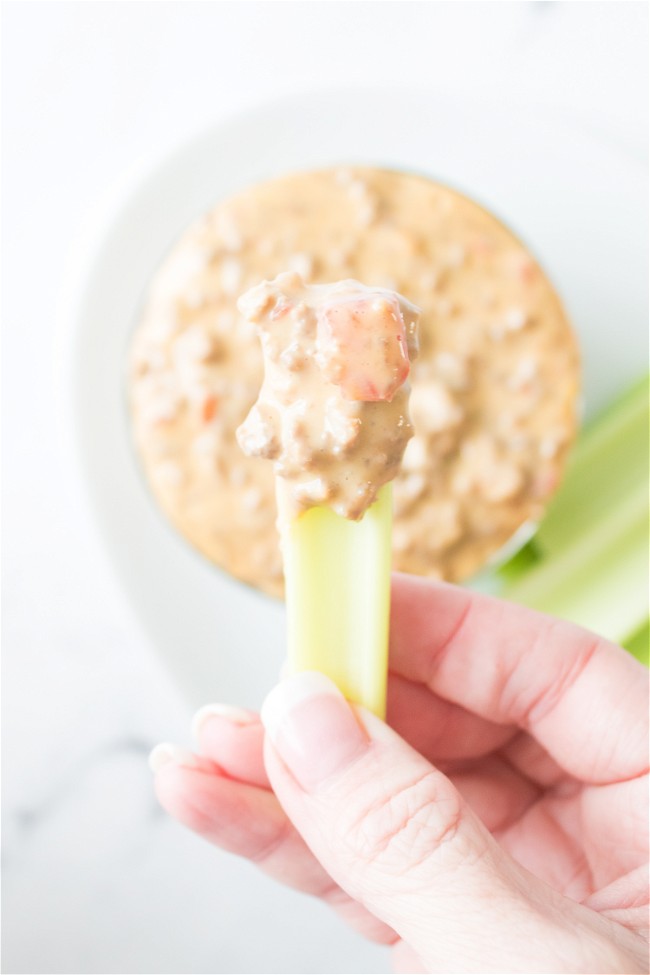 hand holding a piece of celery that has been dipped in rotel cheese dip