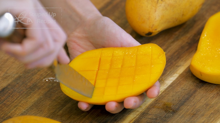 Image of Cut out 3 ripe mangos. Slice the mango down slightly off the center on both sides. Use a pairing knife to score the flesh, but don't cut through the skin.
