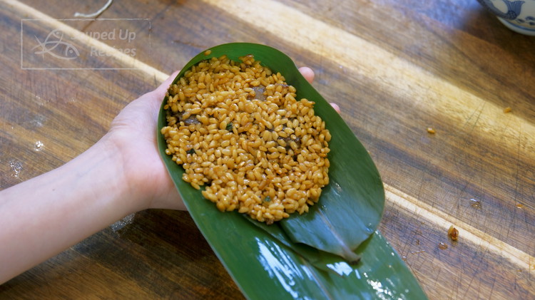 Image of Each zongzi needs two pieces of bamboo leaves. Partially stack them together with the smooth side facing up. The pointy tips should be in the middle. Flip the leaves at 1/3 of the length and fold the sides at 1.4 of...