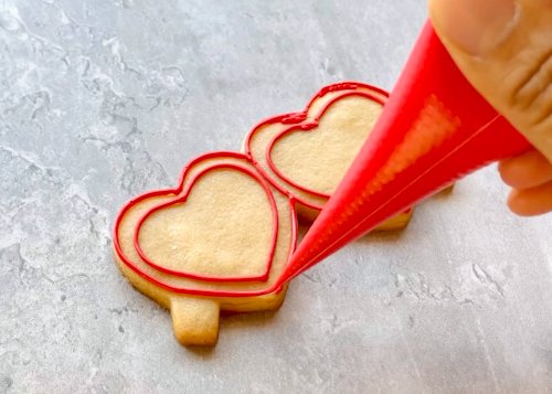 Image of Now, outline the edge of the cookie with red outline consistency icing. This will be the frames of the sunglasses.  