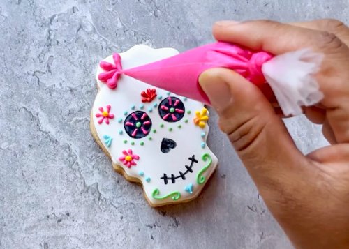 Image of Continue creating a colorful flower crown by piping a large pink flower on the wavy right side of the skull. Follow the lines of the skull as a guide for piping flowers. 